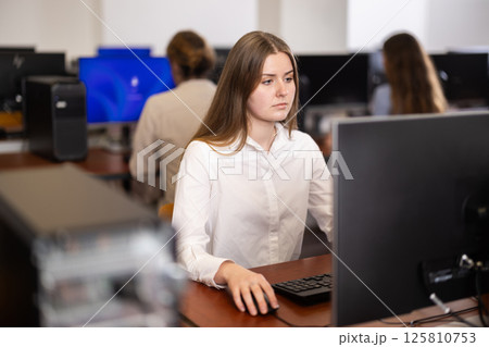 Young woman student of computer courses looks at monitor screen, types on keyboard and does work 125810753