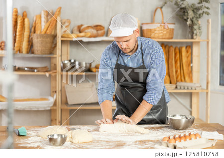 Guy works in bakery as baker, kneads dough, works with flour. Guy works in bakery as baker, kneads dough, works with flour. 125810758