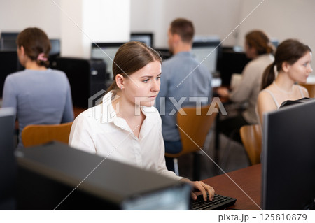 Young woman student of computer courses looks at monitor screen, types on keyboard and does work 125810879
