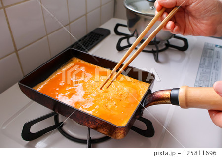 卵を焼く女性の手元	 卵を焼く女性の手元	 125811696
