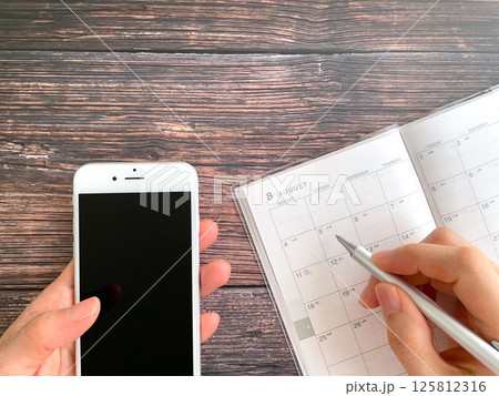 スマホ片手に8月のスケジュール帳に記入する手元 125812316