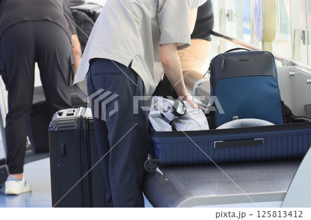 空港の出発ロビーでスーツケースの荷物を詰め替える外国人観光客 125813412