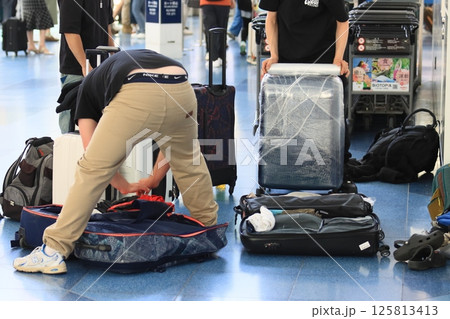空港の出発ロビーでスーツケースの荷物を詰め替える外国人観光客 125813413