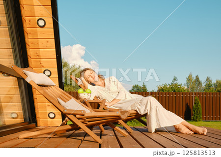 Woman dreaming on folding wooden sun lounger on terrace of tiny house 125813513