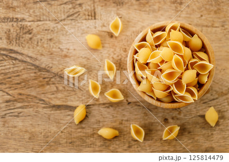 Raw uncooked dried Conchiglie shell pasta. Italian seashells pasta in wooden bowl on wooden background. 125814479