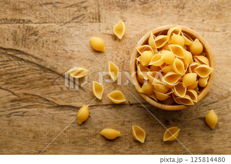 Raw uncooked dried Conchiglie shell pasta. Italian seashells pasta in wooden bowl on wooden background. 125814480