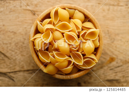 Raw uncooked dried Conchiglie shell pasta. Italian seashells pasta in wooden bowl on wooden background. 125814485