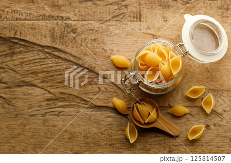 Raw uncooked dried Conchiglie shell pasta. Italian seashells pasta in lock lid glass jar on wooden background. 125814507