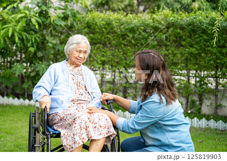 Caregiver help and care Asian senior woman patient sitting on wheelchair in park. Caregiver help and care Asian senior woman patient sitting on wheelchair in park. 125819903