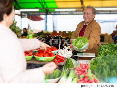 Positive mature casual salesman passing lettuce salad through counter to buyer at bazaar Positive mature casual salesman passing lettuce salad through counter to buyer at bazaar 125820340