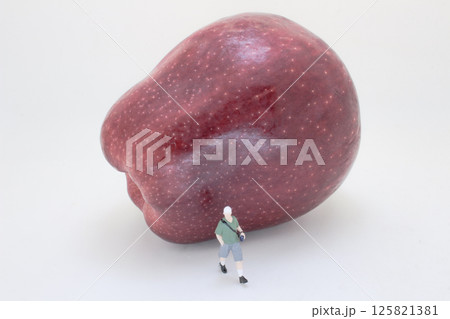Miniature Figure Strolling Alongside a Gigantic Red Apple 125821381