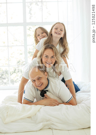 Happy parents and their daughter having fun on a bed indoors Happy parents and their daughter having fun on a bed indoors 125821498