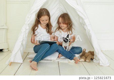 Children friends using tablet gadget and embracing little dog pet on floor at home 125821873