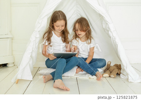 Playful little girl sisters with tablet pc computer in kids tent at home.  125821875