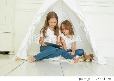 Cheerful child sisters using tablet computer sitting on floor at home 125821876