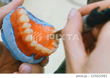 A skilled dental technician meticulously shapes wax into detailed dentures 125822091