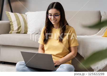 Remote growth and self-reflection. Young Latina Indian woman in her 20s using laptop on sofa for online therapy or studying, balancing mental health and education in a relaxed home vibe 125822299