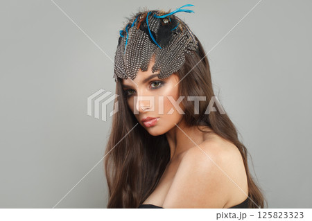 Elegant healthy woman with makeup, long brown curly hair and hair deco feathers accessories 125823323