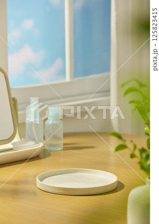 Empty stone pedestal is placed in the middle of the brown table. Cosmetic bottles and cotton pads are displayed next to the table mirror. The window has a view of the blue sky and clouds outside. Empty stone pedestal is placed in the middle of the brown table. Cosmetic bottles and cotton pads are displayed next to the table mirror. The window has a view of the blue sky and clouds outside. 125823415