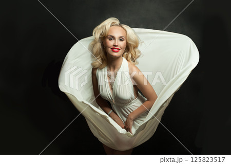 Fashionable woman with blonde hair in white silky dress on black background. Beautiful blond lady  125823517