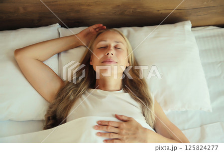 Woman sleeping lying in bed on white soft comfortable pillow in bedroom at home 125824277