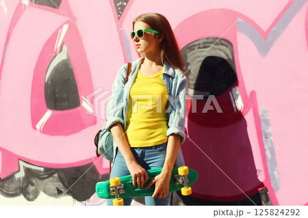 Stylish young girl with skateboard in glasses, modern teenager girl posing against the graffiti wall 125824292