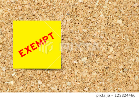 Yellow note paper with word exempt on cork board background with copy space 125824466