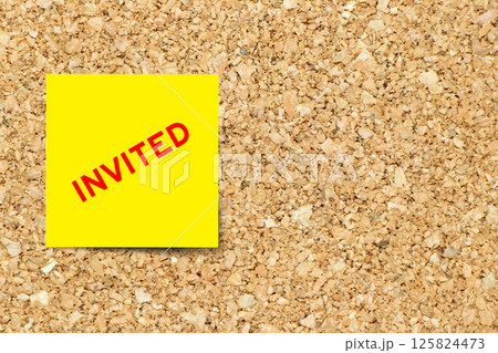 Yellow note paper with word invited on cork board background with copy space Yellow note paper with word invited on cork board background with copy space 125824473
