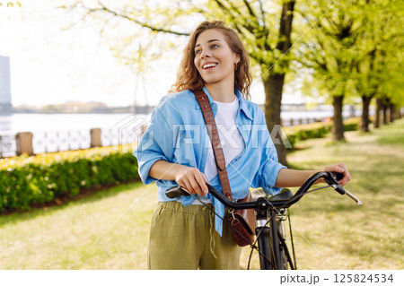 Smiling woman riding bicycle on sidewalk in city spring park. Active urban lifestyle concept. Smiling woman riding bicycle on sidewalk in city spring park. Active urban lifestyle concept. 125824534