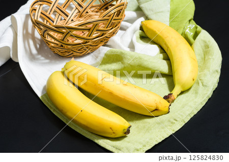 Ripe yellow bananas on a green and white cloth with a wicker basket. 125824830