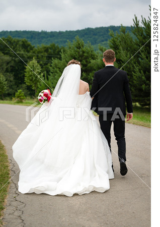 Bride and groom walking away down a path, towards a scenic landscape. 125824847
