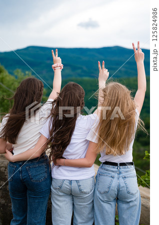 Three friends enjoying a mountain view, arms raised in victory. 125824986