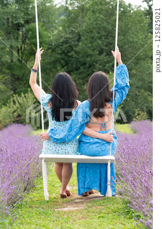 Two girls in a pink dress on a swing, surrounded by lavender. Two girls in a pink dress on a swing, surrounded by lavender. 125825021