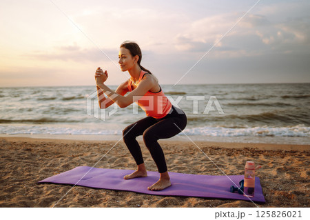 Modern young woman doing yoga on beach at sunrise. Concept of an active lifestyle, yoga or fitness. 125826021
