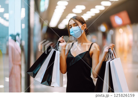 Fashionable woman in protective medical mask with shopping bags walking in the mall. Covid-19. Fashionable woman in protective medical mask with shopping bags walking in the mall. Covid-19. 125826159