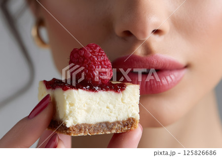 Cheesecake slice with raspberry near womans lips Cheesecake slice with raspberry near womans lips 125826686