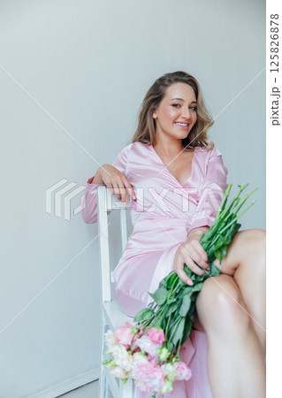 woman in summer pink dress with bouquet of spring flowers sitting on chair 125826878