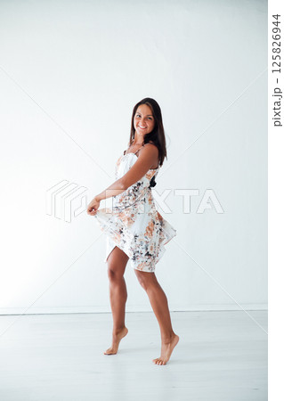 woman in summer dress dancing to music in white room 125826944