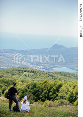 Two tourists looking at the green forest from the top of the mountain Two tourists looking at the green forest from the top of the mountain 125826974
