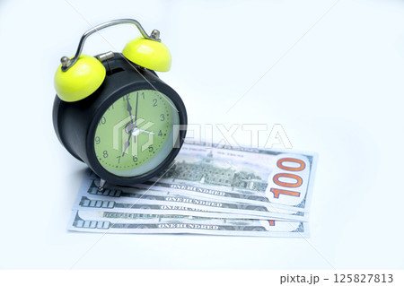 Green alarm clock and a pile of 100 dollar banknotes on a white background. Concept of time is money, saving or investment, and tax 125827813