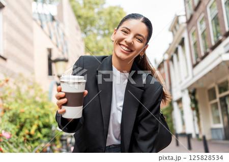 Chic young woman in black suit enjoying coffee on a sunny city stroll, ideal for concepts of weekend leisure, modern fashion, urban lifestyle, or personal branding Chic young woman in black suit enjoying coffee on a sunny city stroll, ideal for concepts of weekend leisure, modern fashion, urban lifestyle, or personal branding 125828534