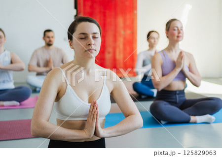 Yoga mindfulness meditation. Group of sporty people doing exercise in studio for class for yoga wellness mindfulness meditation. Men women practicing yoga sitting in lotus pose meditating relaxing 125829063