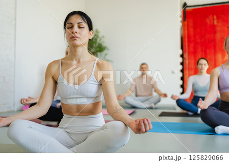 Yoga mindfulness meditation. Group of sporty people doing exercise in studio for class for yoga wellness mindfulness meditation. Men women practicing yoga sitting in lotus pose meditating relaxing Yoga mindfulness meditation. Group of sporty people doing exercise in studio for class for yoga wellness mindfulness meditation. Men women practicing yoga sitting in lotus pose meditating relaxing 125829066