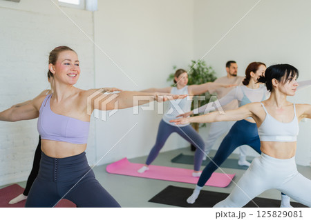 Yoga class Pilates workout. Group of sporty people doing exercise in studio class for yoga wellness mindfulness meditation. Personal trainer men women practicing yoga in gym training stretching indoor Yoga class Pilates workout. Group of sporty people doing exercise in studio class for yoga wellness mindfulness meditation. Personal trainer men women practicing yoga in gym training stretching indoor 125829081