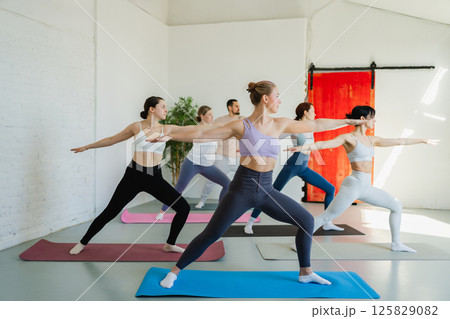 Yoga class Pilates workout. Group of sporty people doing exercise in studio class for yoga wellness mindfulness meditation. Personal trainer men women practicing yoga in gym training stretching indoor 125829082
