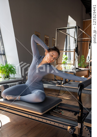 Woman doing mermaid exercise in a sunlite, modern pilates studio, embodying calm, focus, and strength. Woman doing mermaid exercise in a sunlite, modern pilates studio, embodying calm, focus, and strength. 125829441