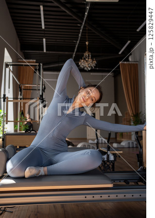 Woman training pilates on the reformer bed. Reformer pilates studio machine for fitness workouts in gym. Fit, healthy and strong authentical body. Fitness concept 125829447