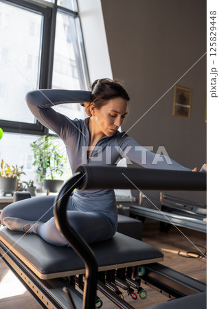Woman training pilates on the reformer bed. Reformer pilates studio machine for fitness workouts in gym. Fit, healthy and strong authentical body. Fitness concept Woman training pilates on the reformer bed. Reformer pilates studio machine for fitness workouts in gym. Fit, healthy and strong authentical body. Fitness concept 125829448