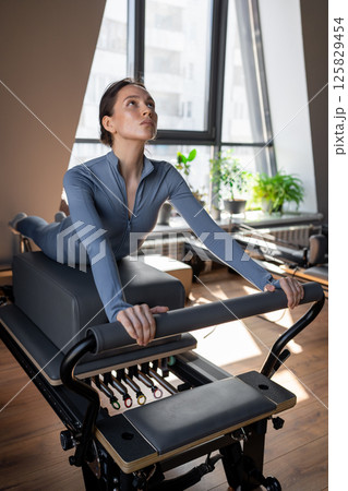Woman training pilates on the reformer bed. Reformer pilates studio machine for fitness workouts in gym. Fit, healthy and strong authentical body. Fitness concept 125829454