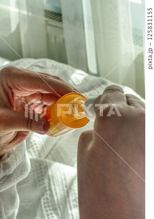 female Hands opening orange skincare serum bottle in cozy morning light on white bed. High quality photo 125831155